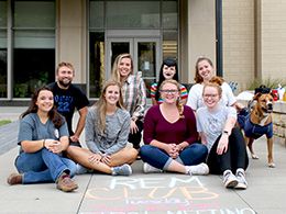 REM student group posing in front of building with REM Club written on sidewalk in front of them